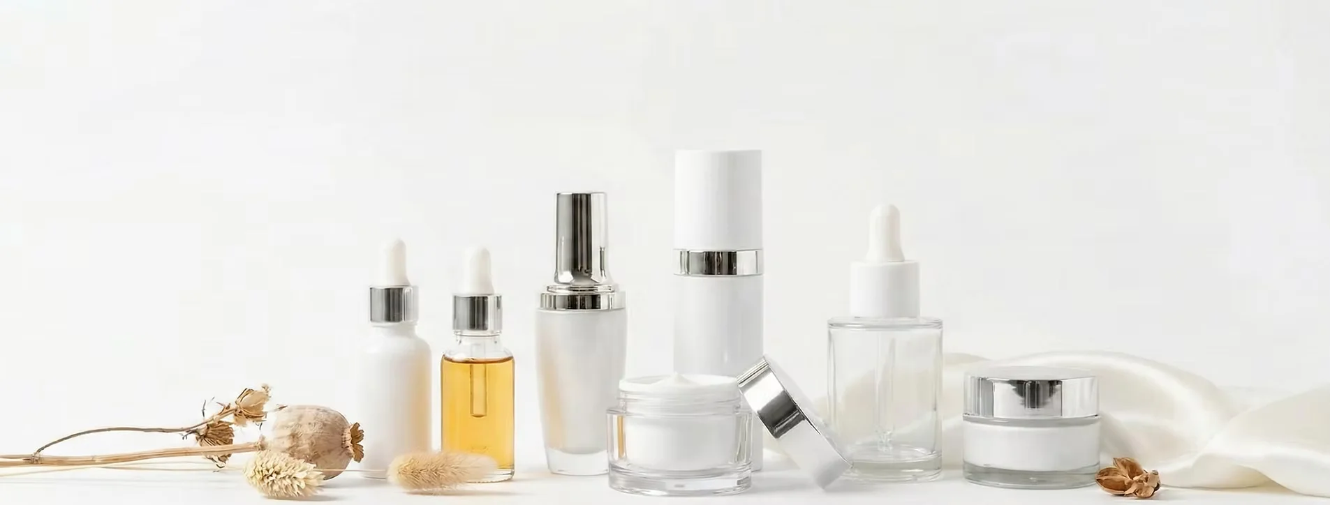 Various skincare products in white and silver packaging with pipettes, creams, and bottles on a white surface.